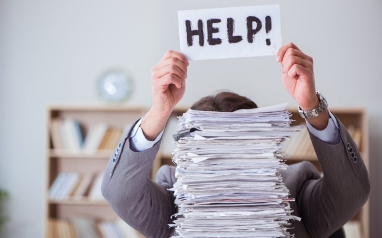 Zakenman verstopt achter berg rapportages en een briefje met help omhoog houdt