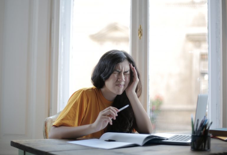 Foto van persoon aan bureau, wrijft over slaap vanwege hoofdpijn