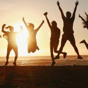 Silhouetten van groep mensen op een rijtje op het strand tijdens ondergaande zon